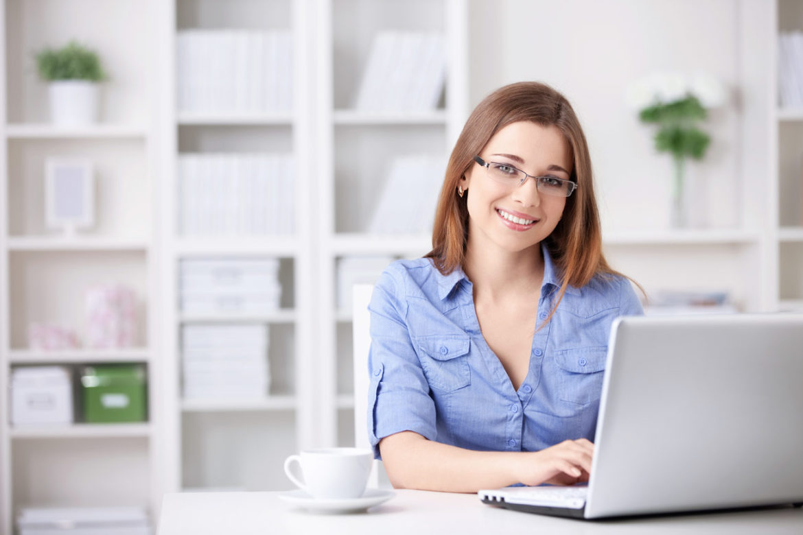 Lächelnde Frau arbeitet am Laptop im hellen Büro – Webseite selbst pflegen mit CMS