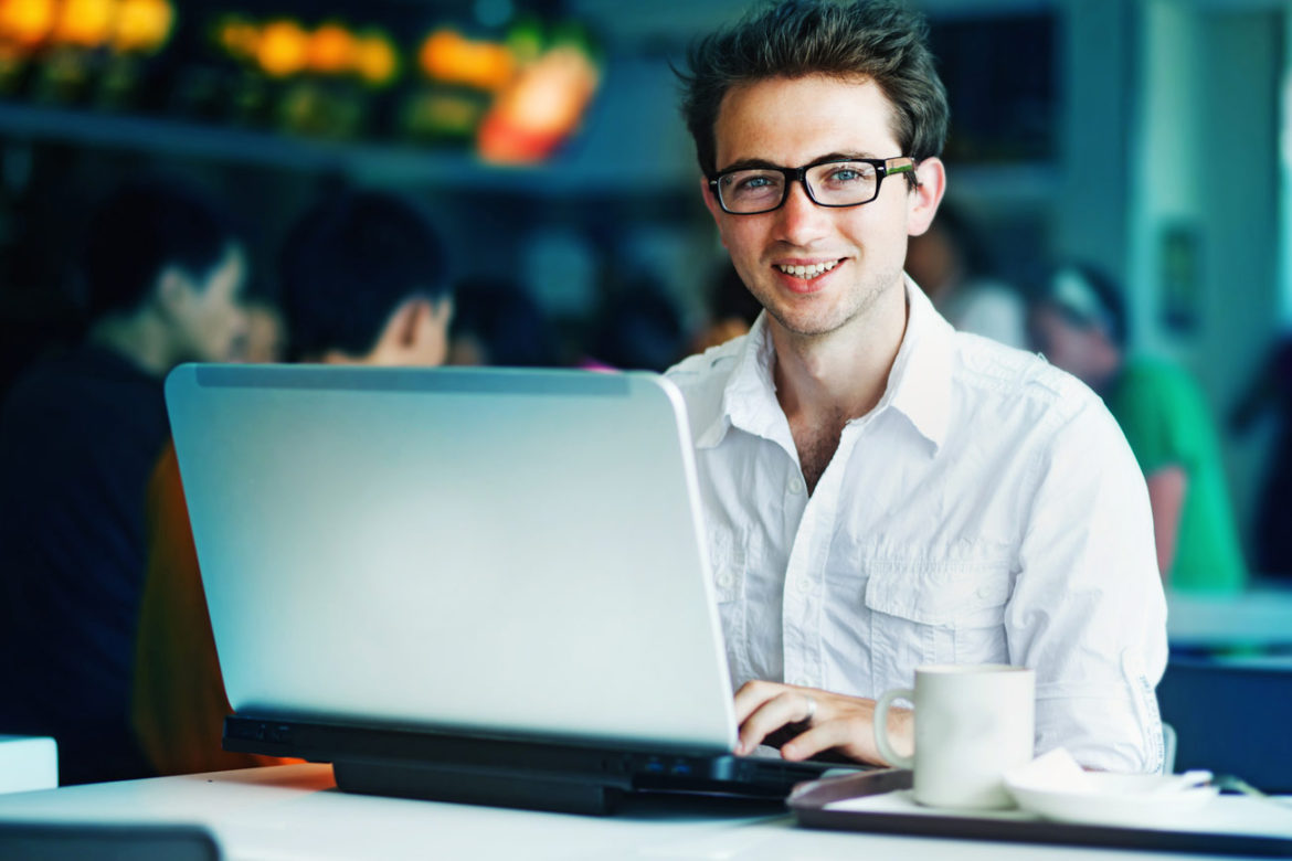 Lächelnder Mann arbeitet im Café am Laptop – die eigene Webseite als günstigste Werbung